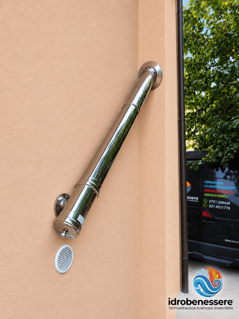 Tubazione in metallo cromato fissata a una parete beige, con una griglia di ventilazione bianca sottostante.